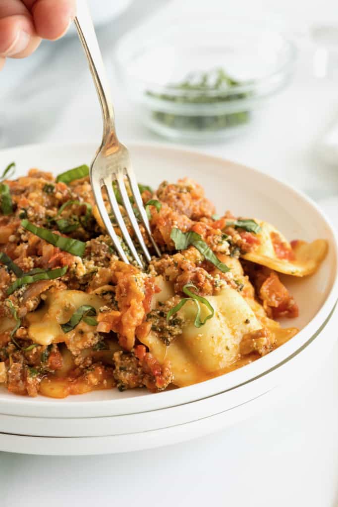 A fork going into a serving of lasagna on a white dinner plate.