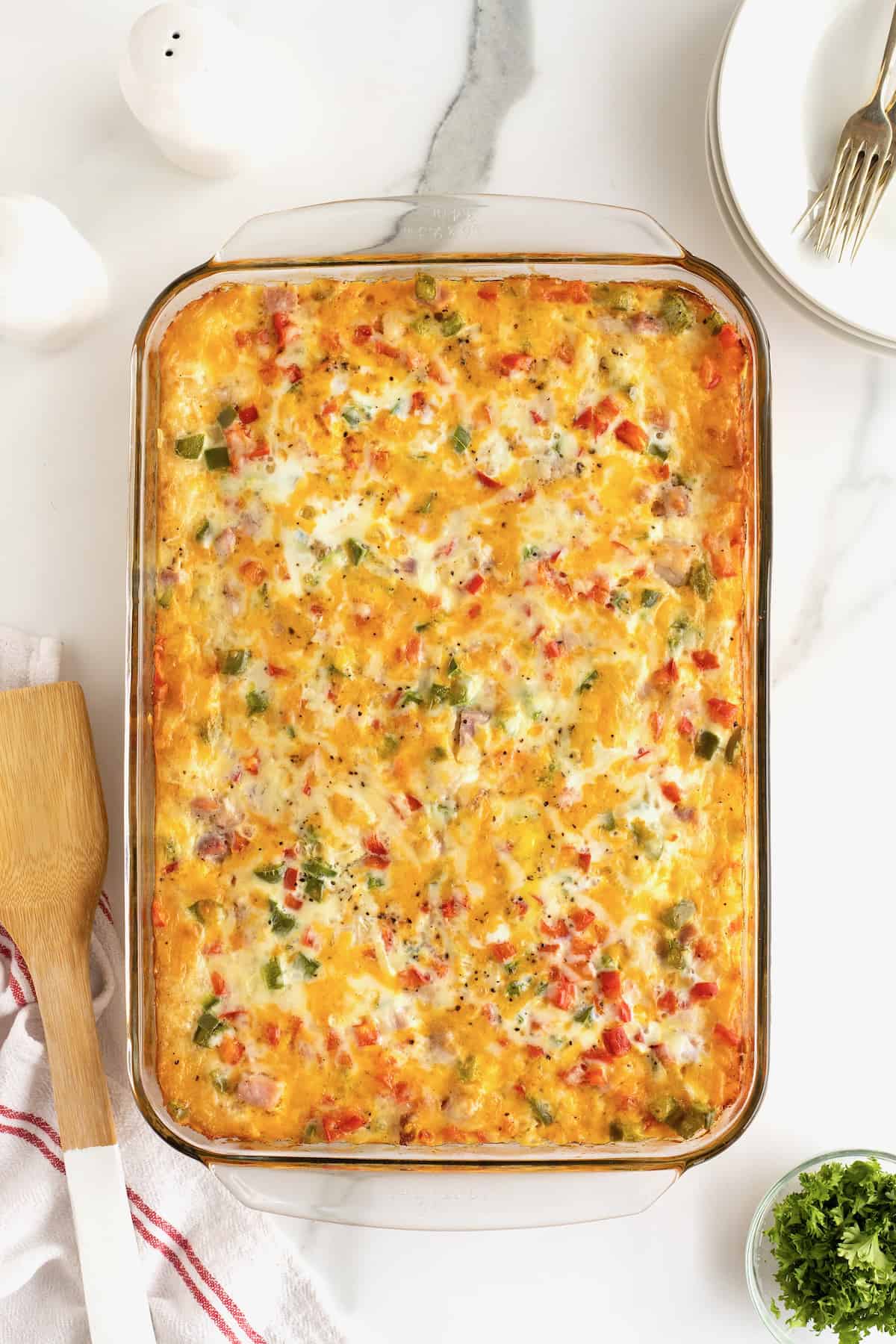 Cooked breakfast casserole in a glass casserole dish with a wooden spatula next to it.