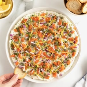 A round white serving platter with cream cheese smoked salmon dip and bagel chips.