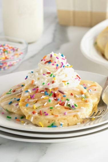 Homemade pancakes with colorful confetti sprinkles, topped with whipped cream and more sprinkles.