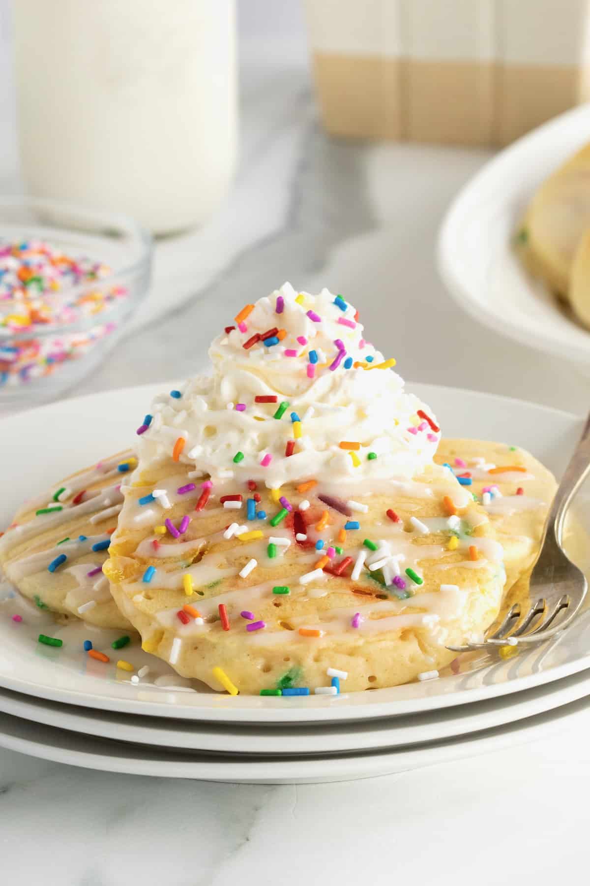 Buttermilk pancakes with colorful confetti sprinkles, topped with whipped cream and more sprinkles.