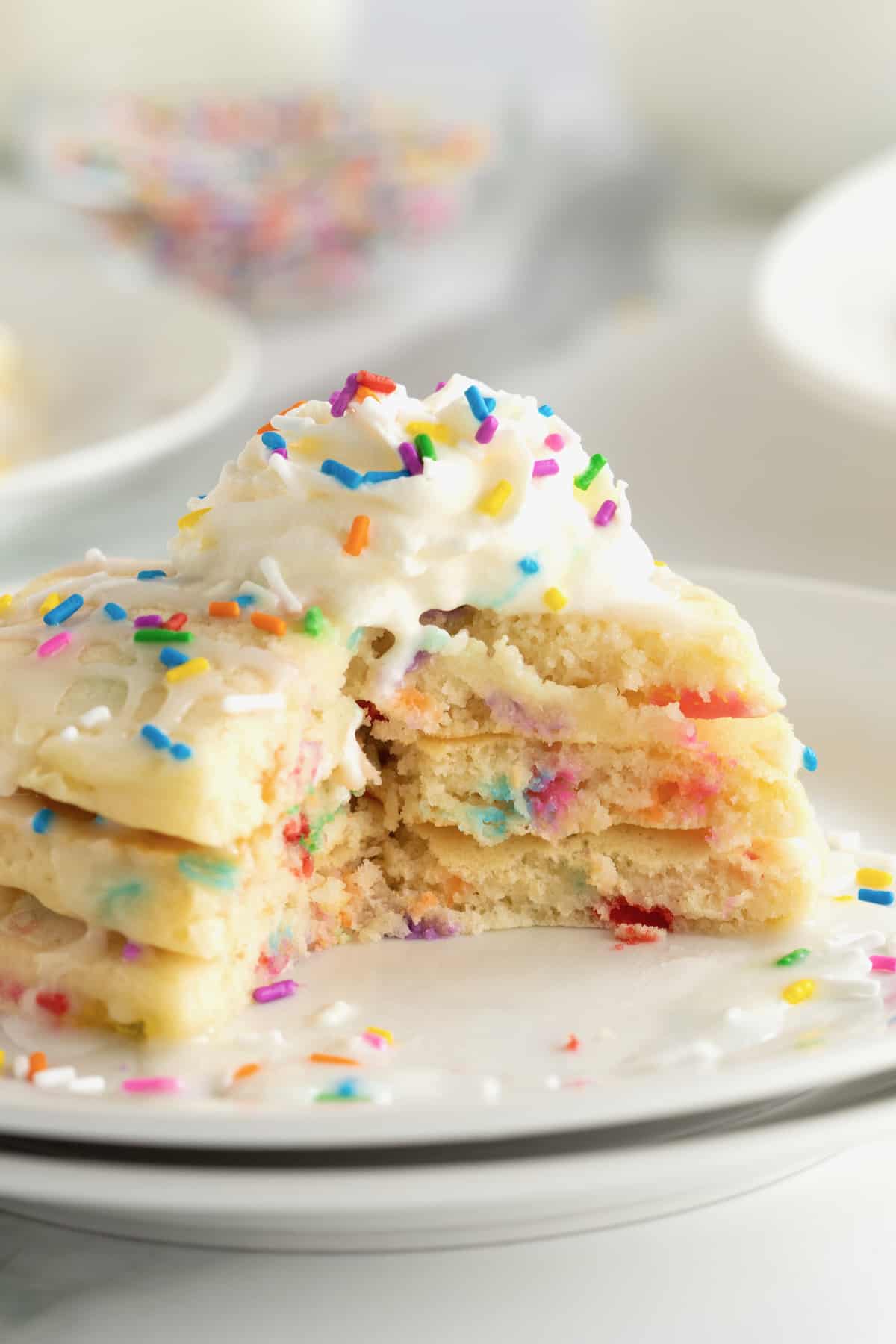 Fluffy pancakes with colorful confetti sprinkles, topped with whipped cream and more sprinkles.