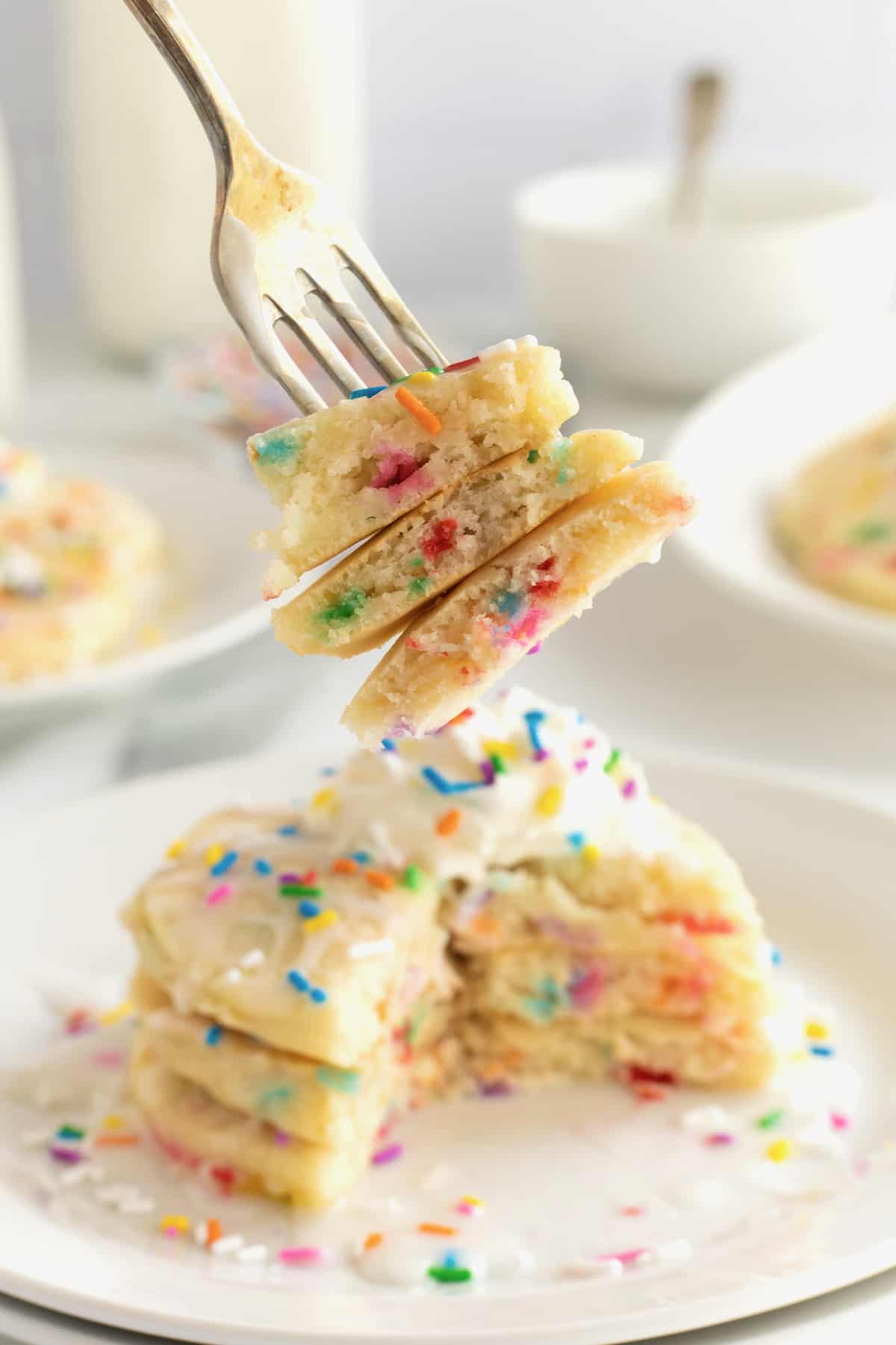 Fluffy pancakes with colorful confetti sprinkles, topped with whipped cream and more sprinkles.
