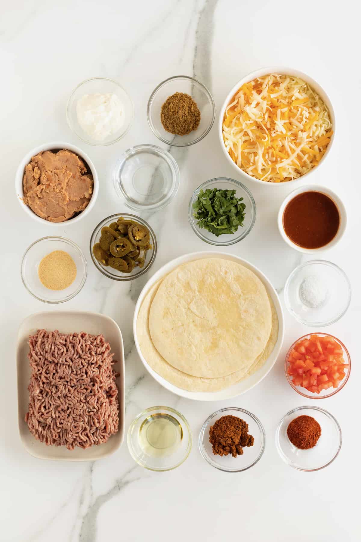 Canola oil, ground beef, chili powder, garlic powder, ground cumin, paprika, kosher salt, water, flour tortillas, refried beans, shredded Monterrey jack and cheddar cheese blend, enchilada sauce, diced fresh tomato, sliced jalapeño peppers, chopped fresh cilantro, sour cream in small glass containers. 
