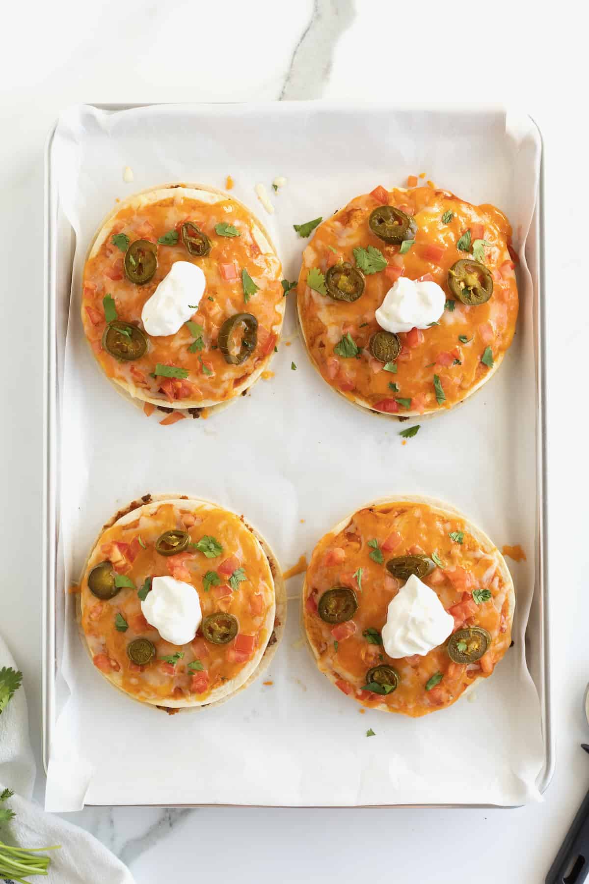 Pizzas made from tortillas with melted cheese, sliced jalapeño, and topped with sour cream.