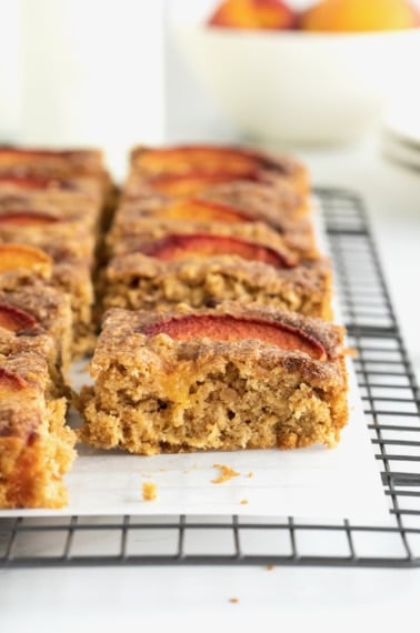 Oatmeal bars with peach slices on top resting on a parchment lined cooling rack.
