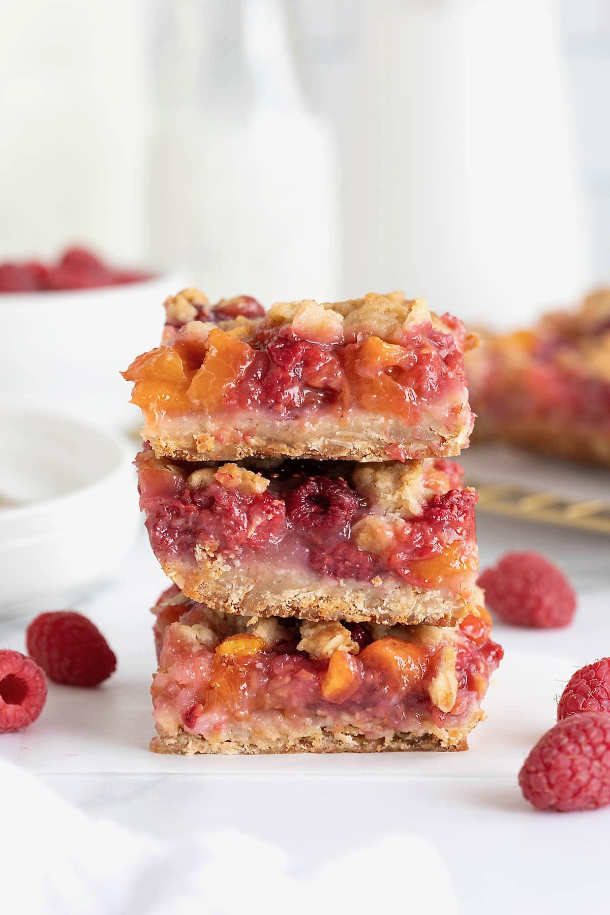 A stack of three peach raspberry crumb bars on a white marble counter. 