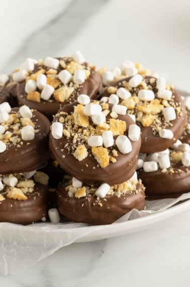 A white serving plate with chocolate covered cracker bites covered in graham cracker bits and mini marshmallows.