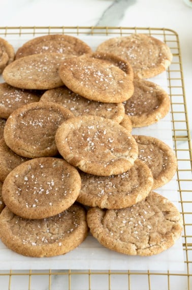 Snickerdoodle cookies sprinkled with sea salt piled on a parchment lined cooling rack.