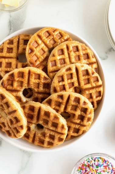 A serving plate full of donut shaped waffles.