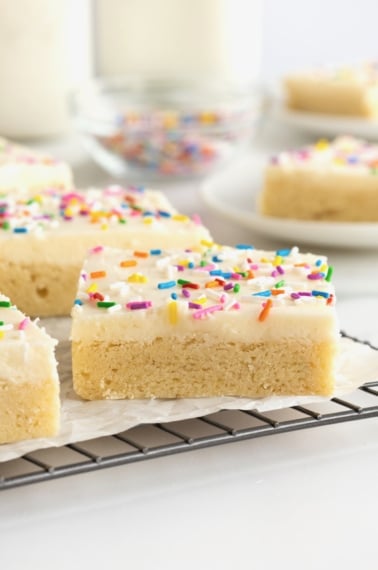 A square sugar cookie bar with white frosting and rainbow sprinkles.
