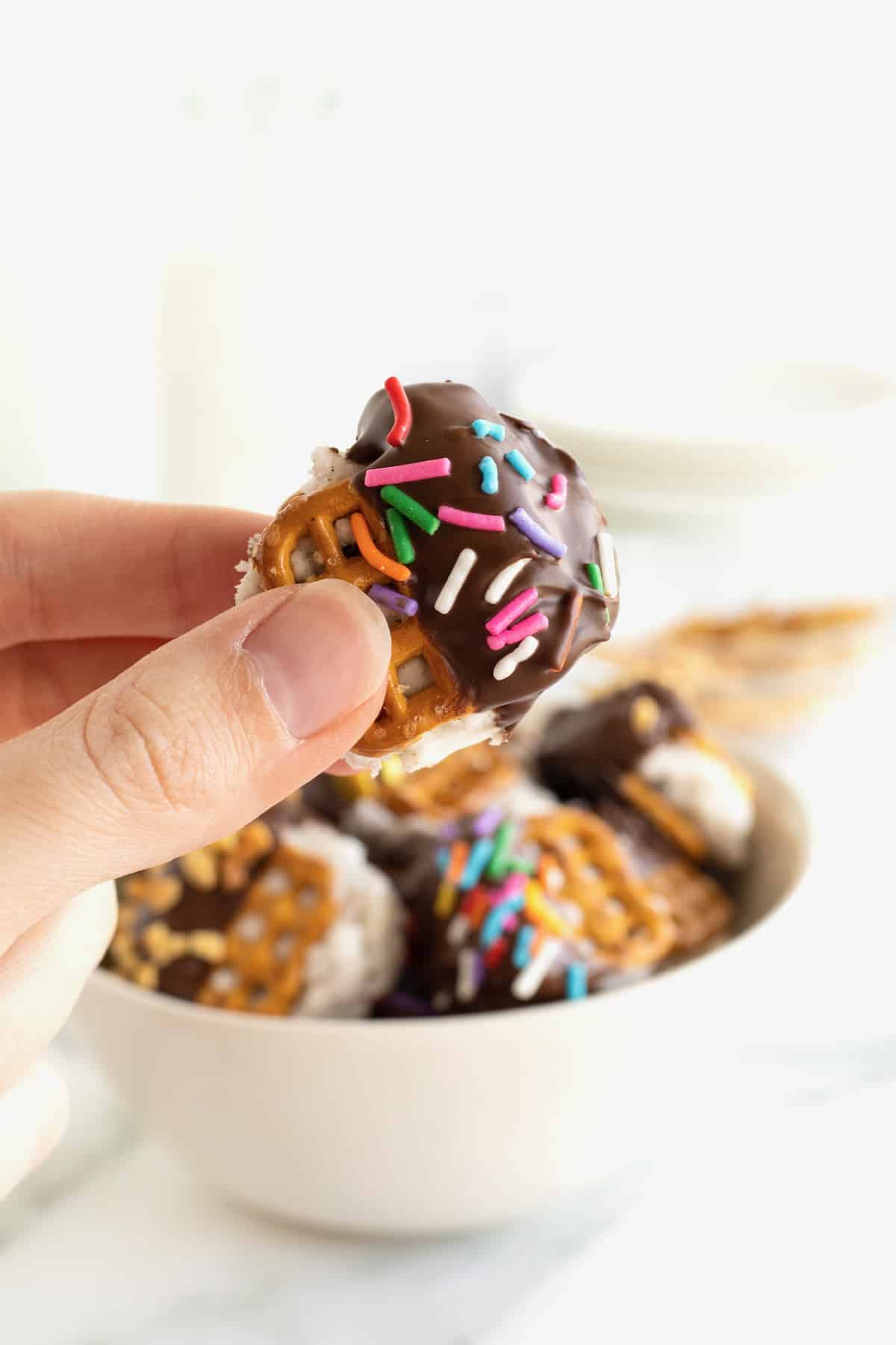 A mini ice cream sandwich made with pretzels and dipped in chocolate and coated in rainbow sprinkles.