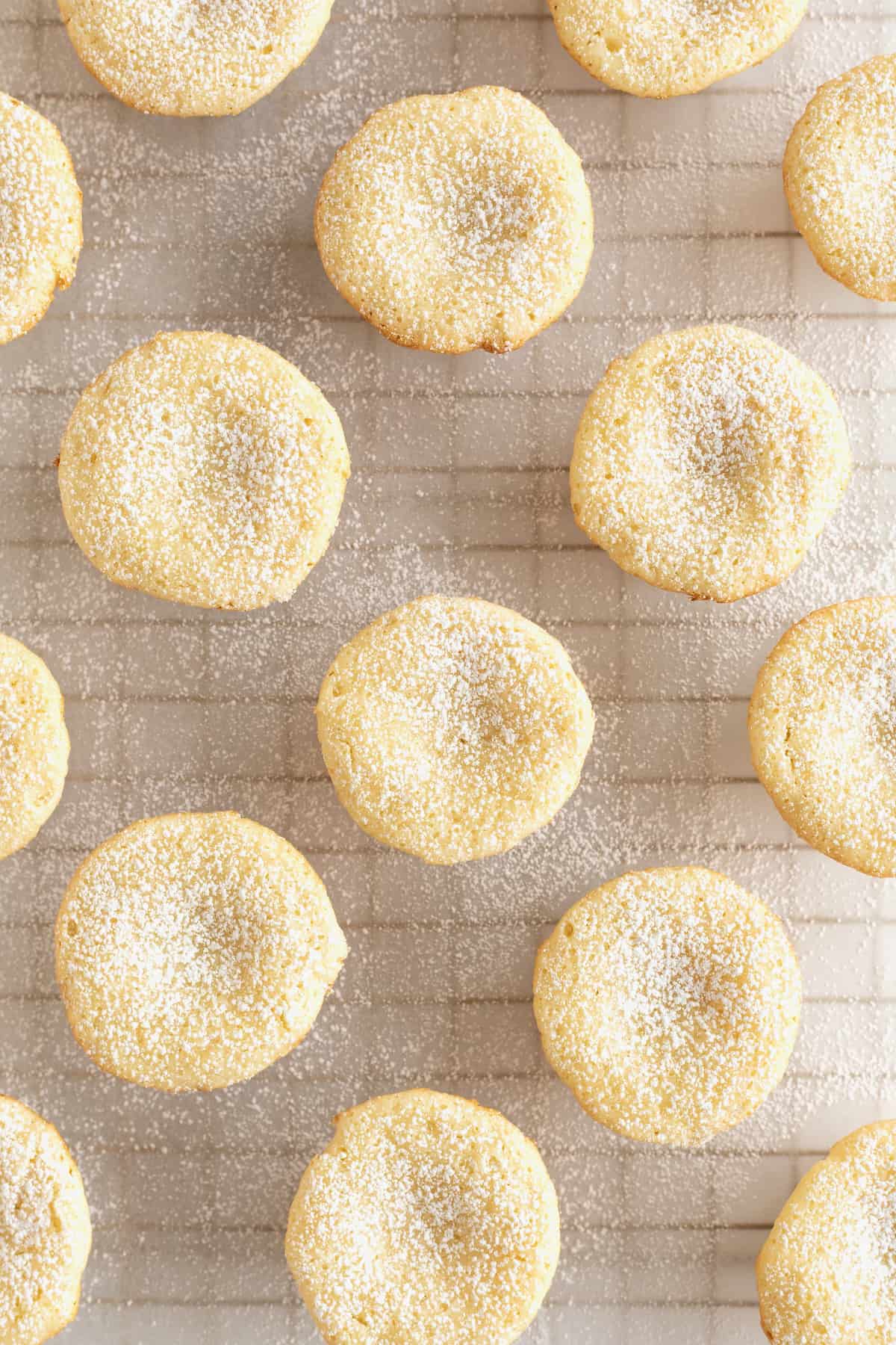 A parchment lined cooling rack with mini gooey butter cakes sprinkled with powdered sugar.