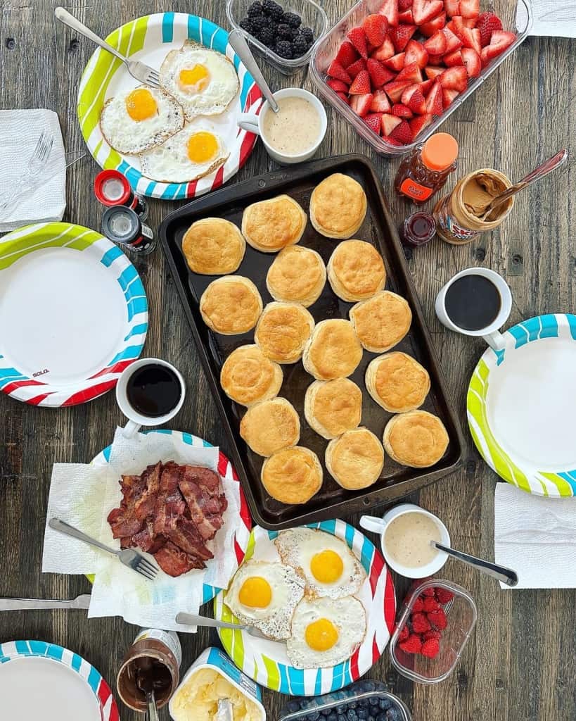Biscuits, fried eggs, bacon and fruit on a wooden table.