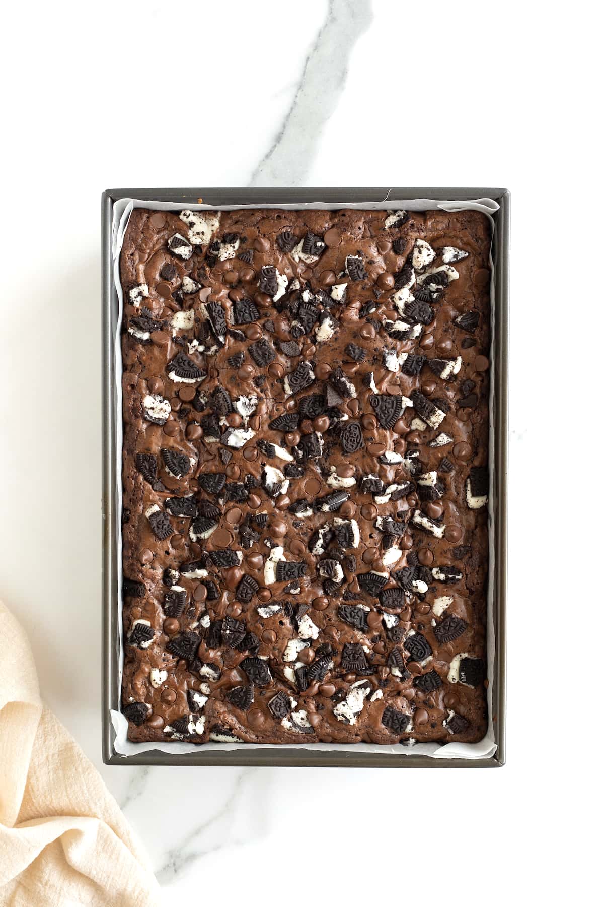 A pan of three layer brownies topped with Oreo pieces and chocolate chips.