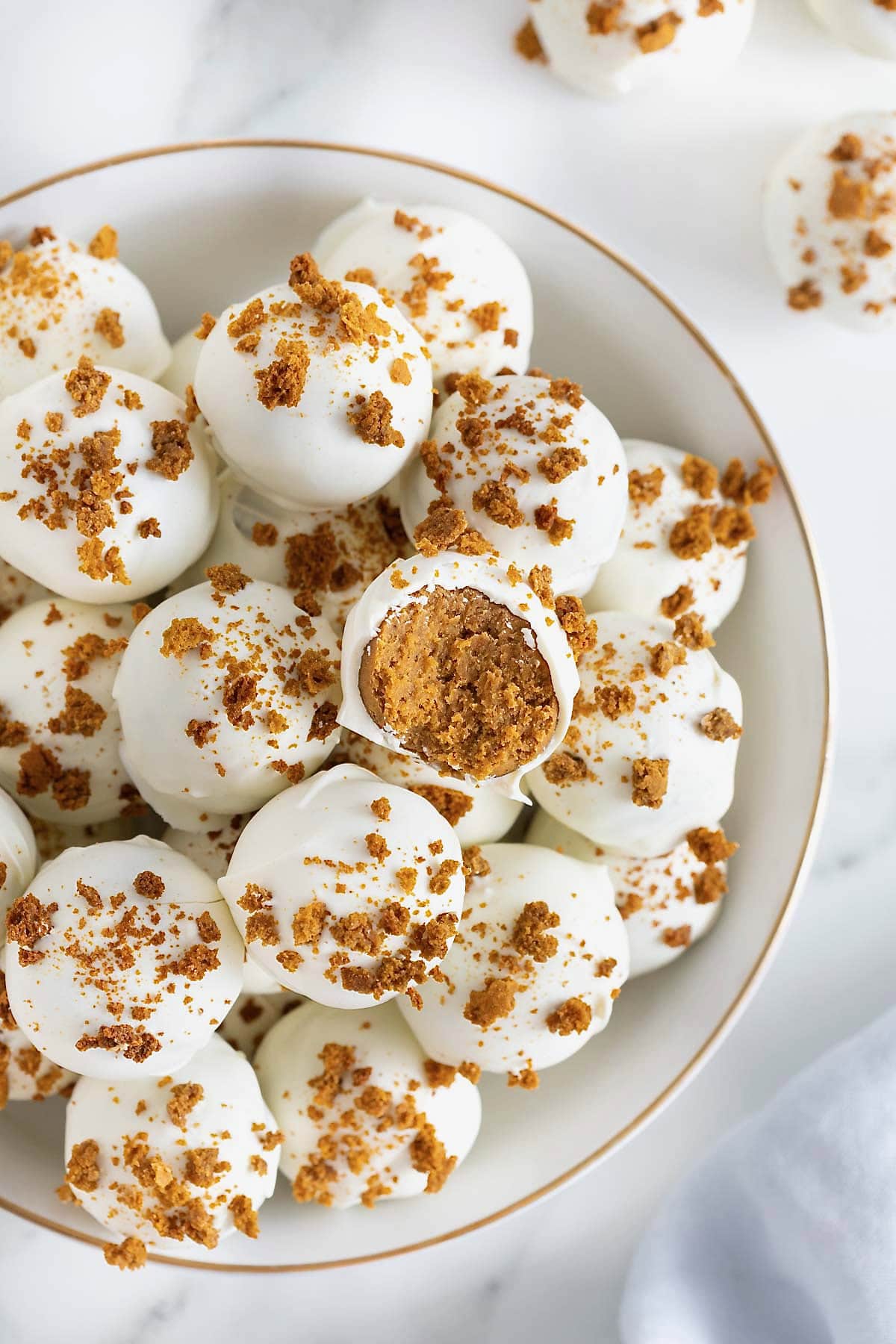 A large white gold-rimmed serving dish filled with pumpkin spice cake balls.
