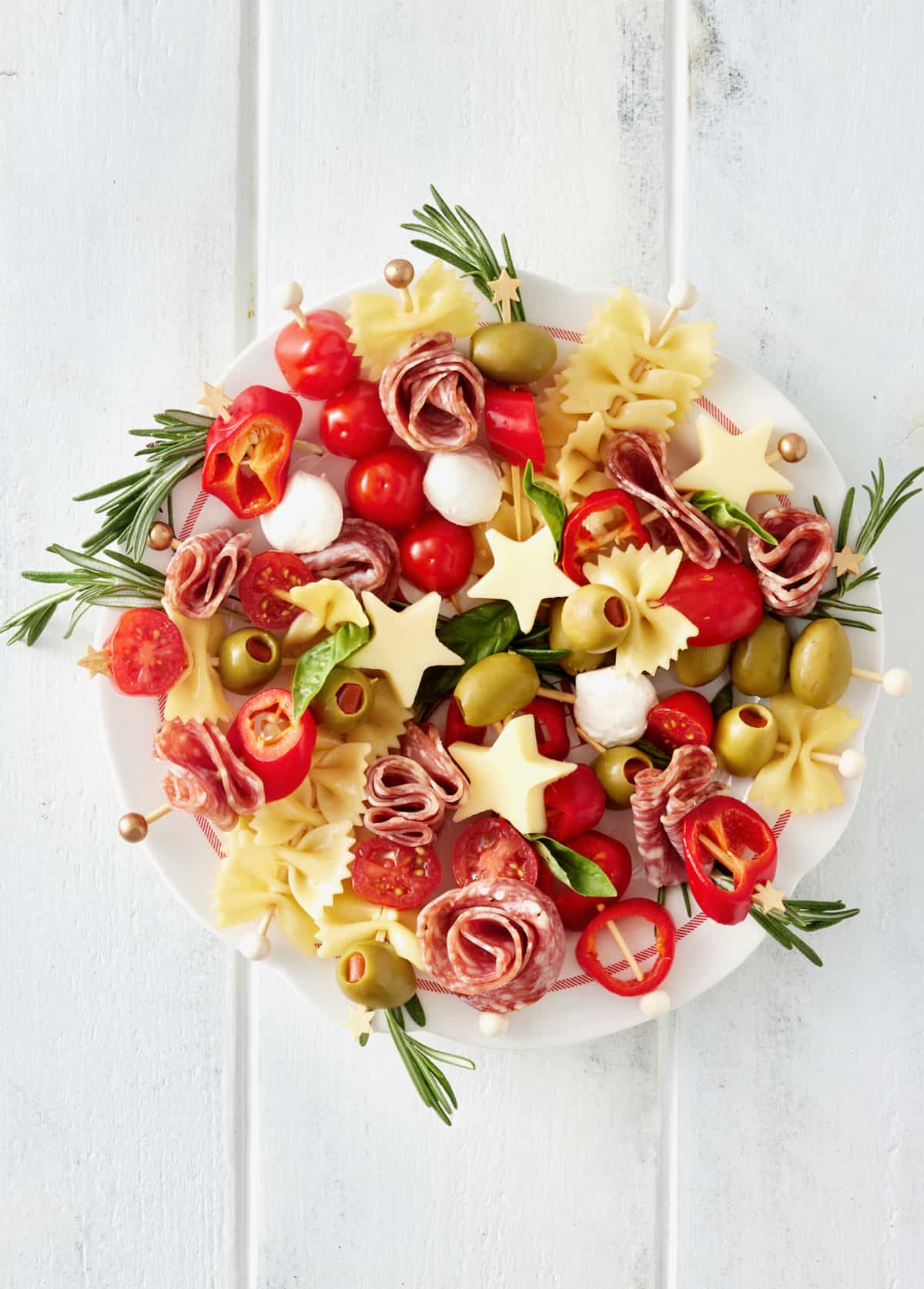 A large white serving plate with skewers made of meats, olives, peppers and cheeses laid out in a circle to look like a holiday wreath.