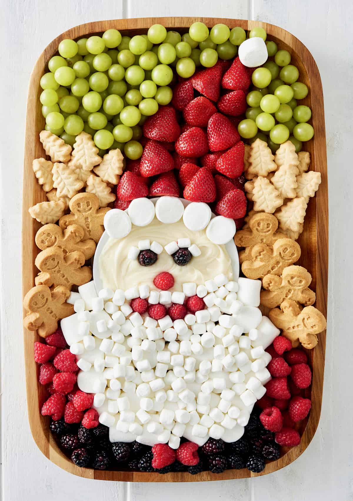 A wood food board decorated with fruit and cookies and marshmallows to look like Santa.