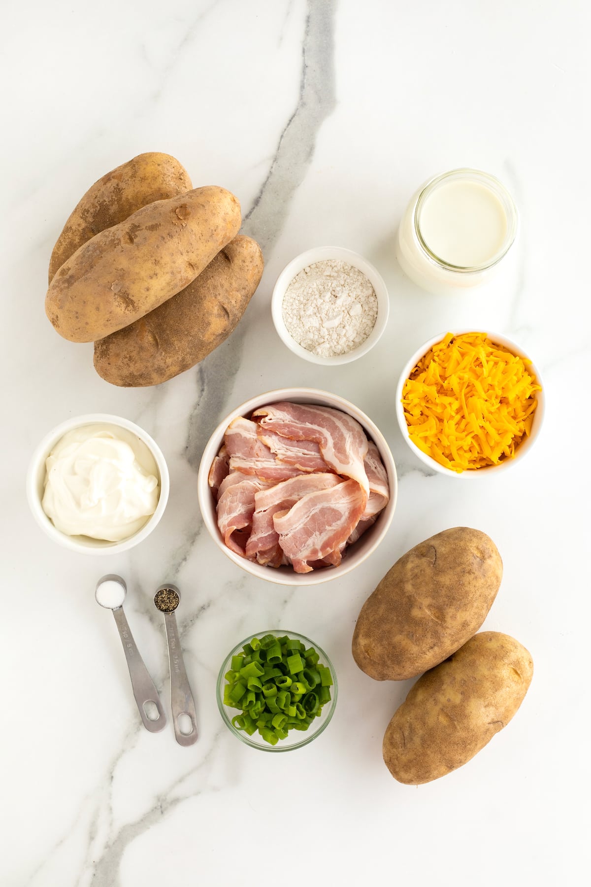 Ingredients for baked potato soup in small white ceramic dishes on a white marble counter.