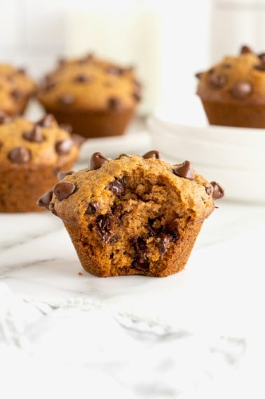 A pumpkin chocolate chip muffin with a bite taken out of it on a white marble counter.