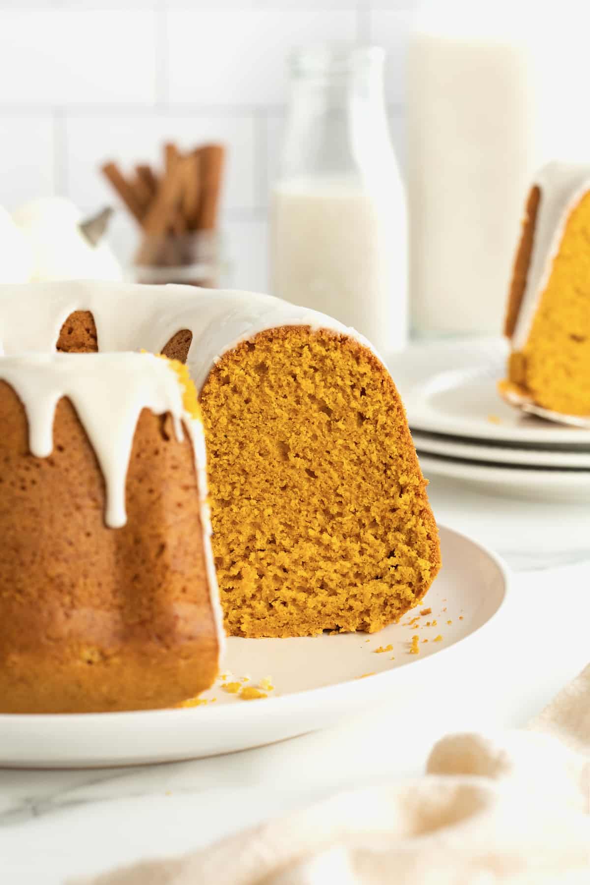 A pumpkin pound cake topped with a white glaze dripping down it on a white serving platter. One slice is missing from the cake.