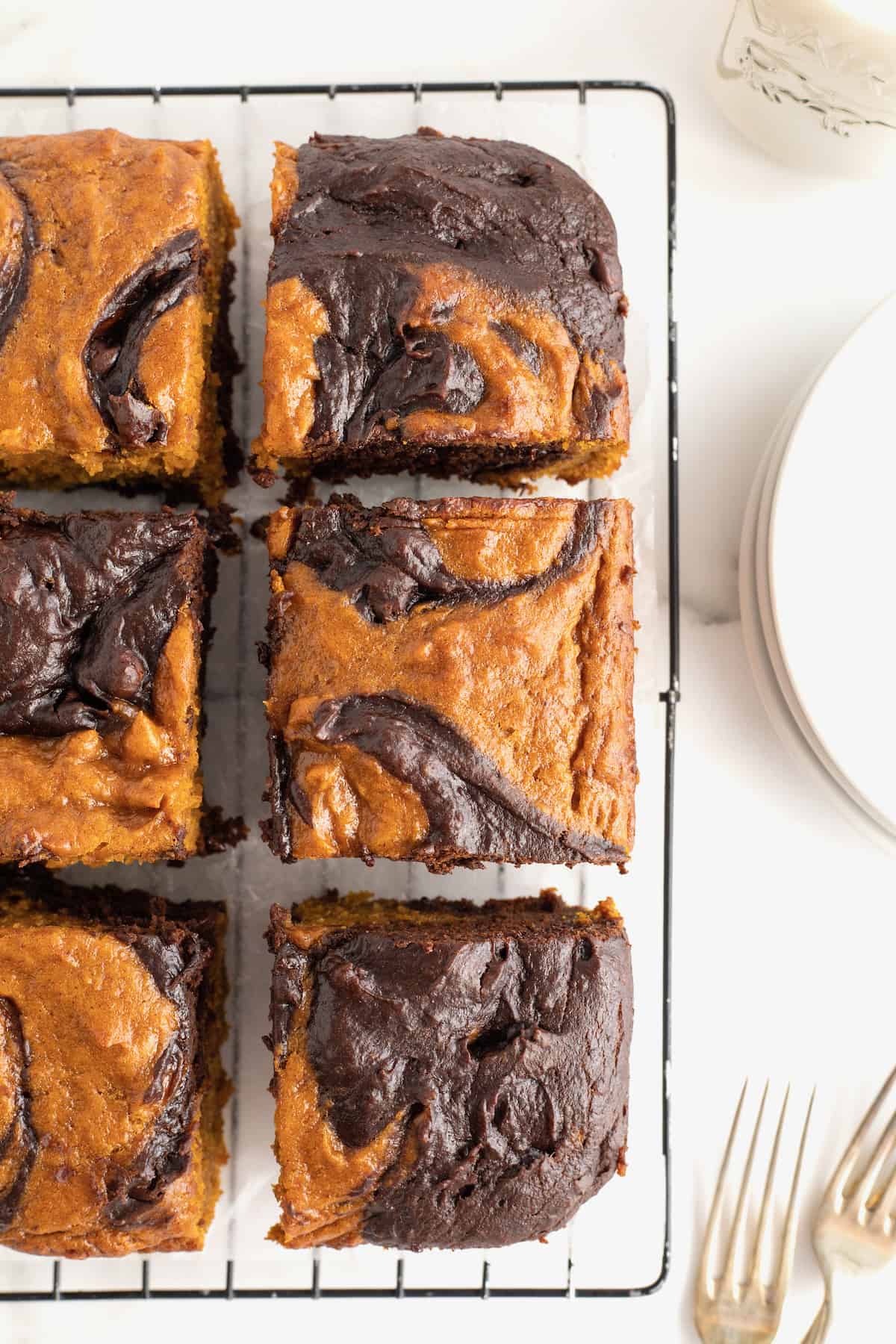 A metal cooking rack with a sheet of parchment covering it with six pumpkin swirled brownies on it.
