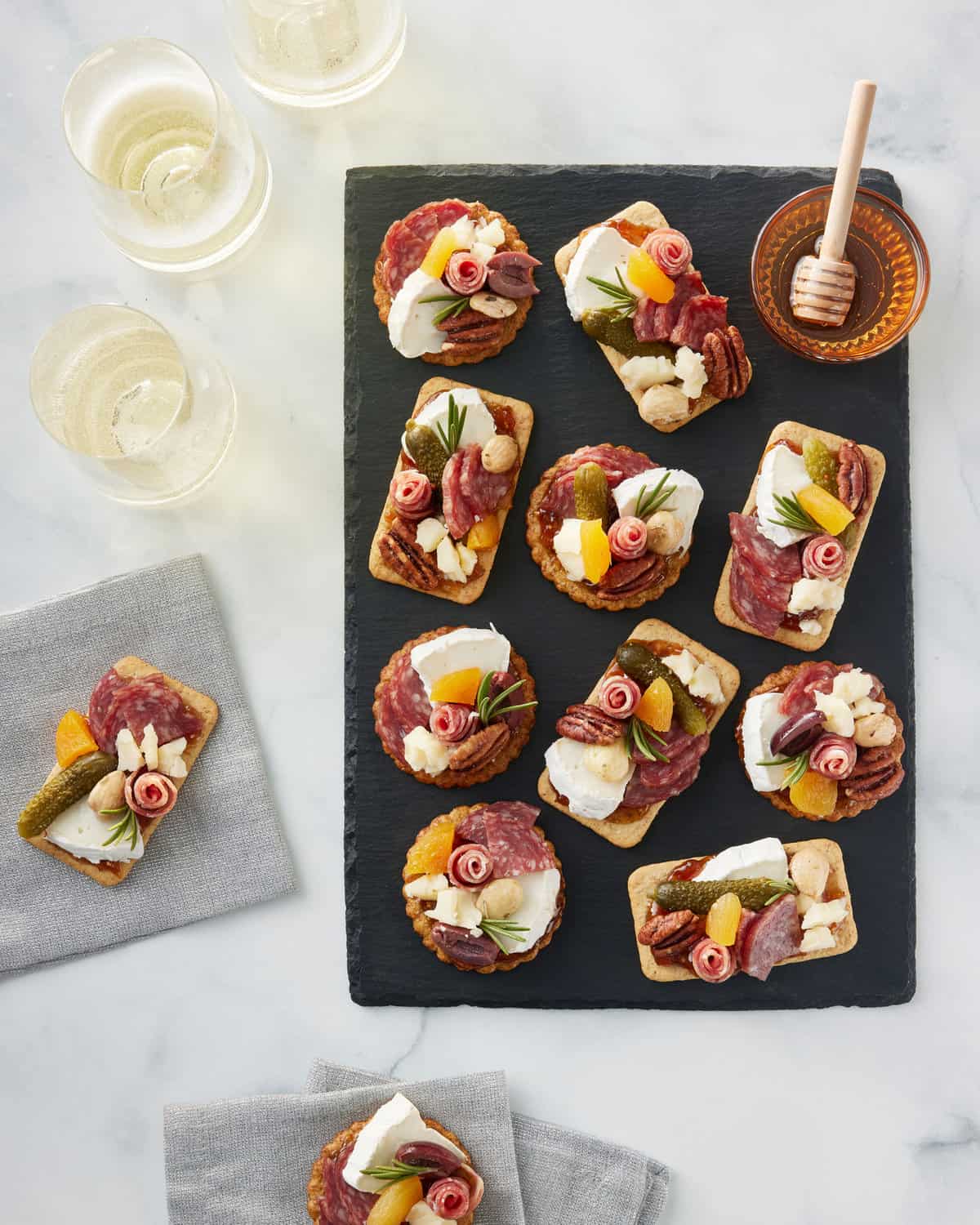 10 round and rectangle shaped crackers topped with tiny bites of cheese, nuts and tiny soprasetta roses.
