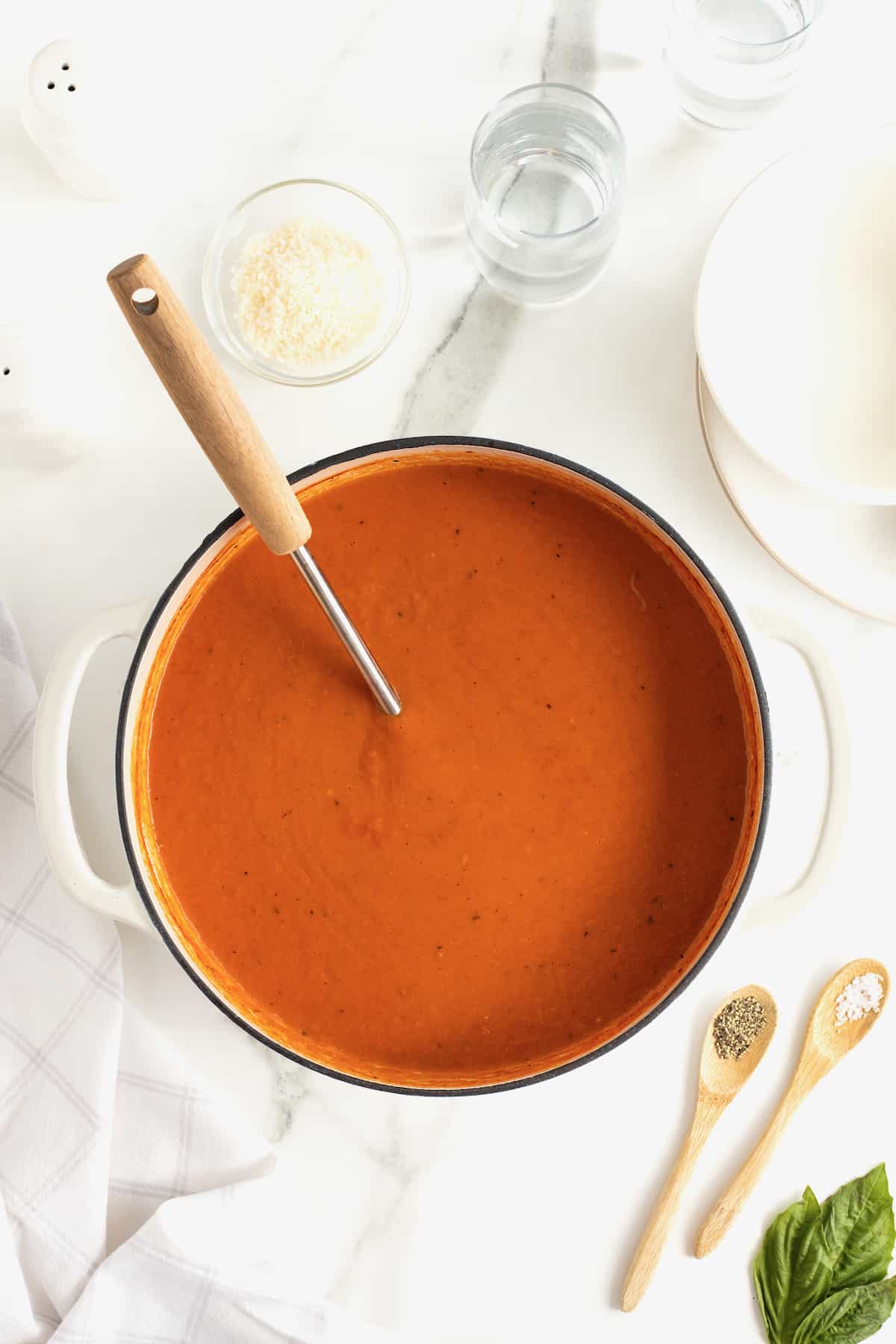 A pot of tomato soup with a wooden ladle handle sticking out.