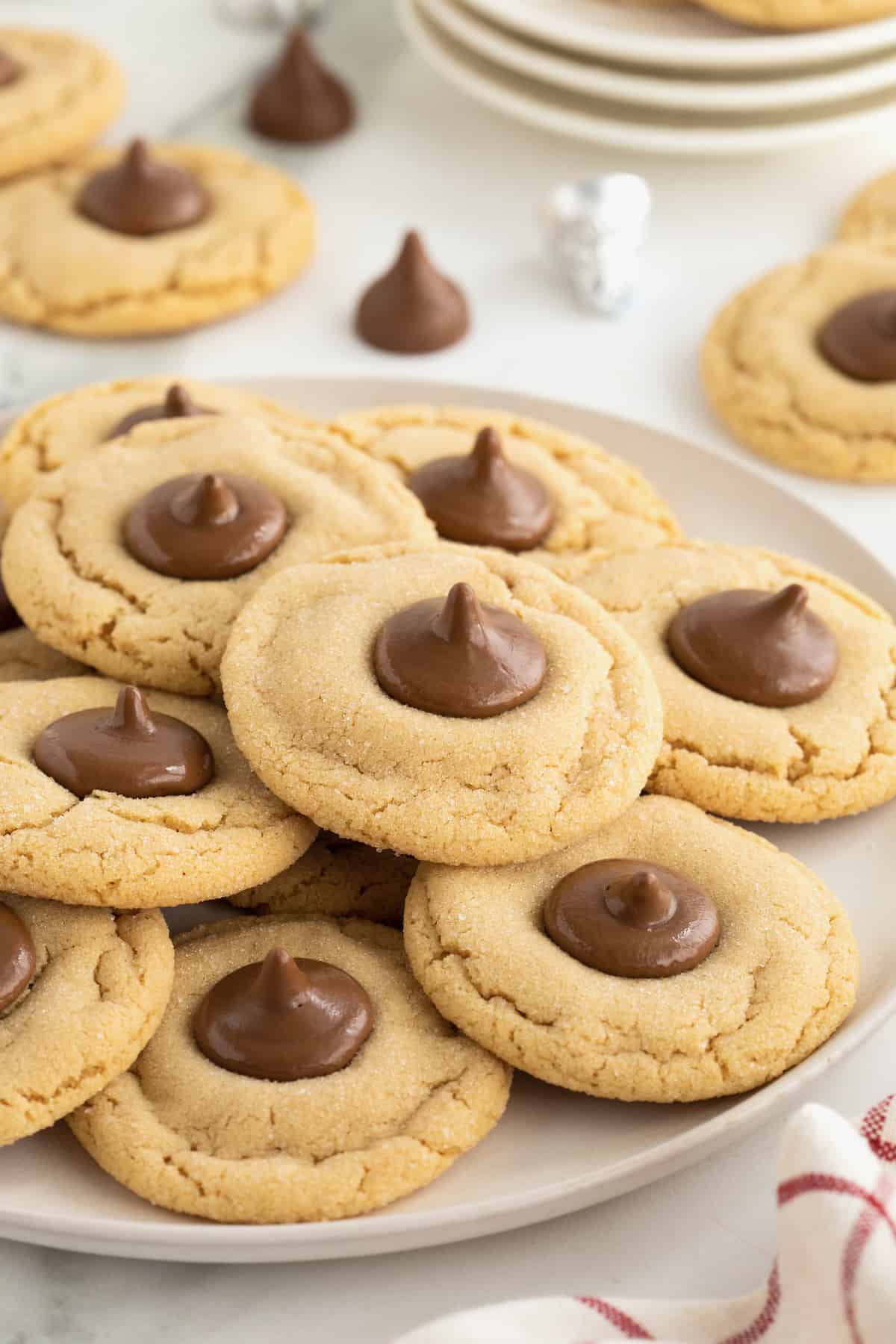 A pile of peanut butter holiday cookies with a Hershey's kiss in the center on a round white serving plate.