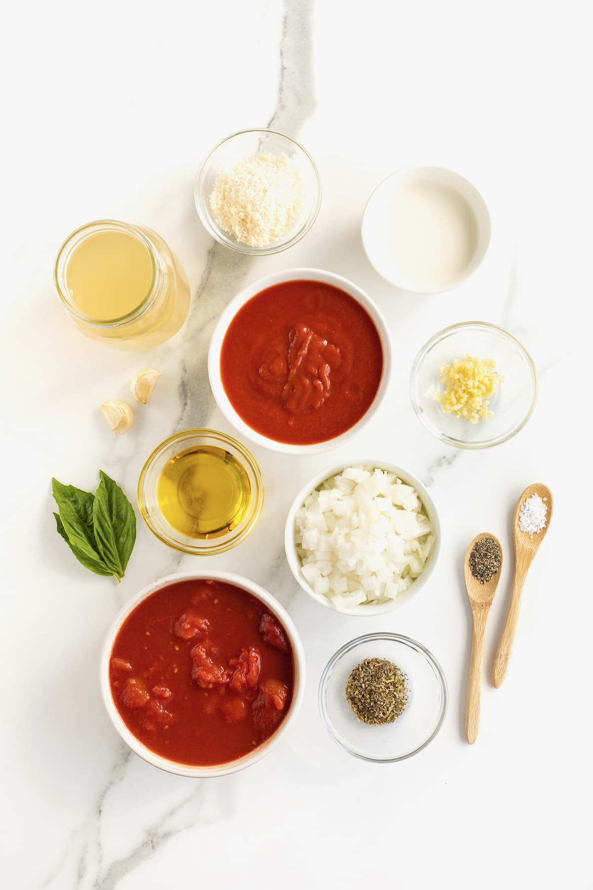 All the ingredients of making homemade tomato soup in small white glass dishes on a white counter top.