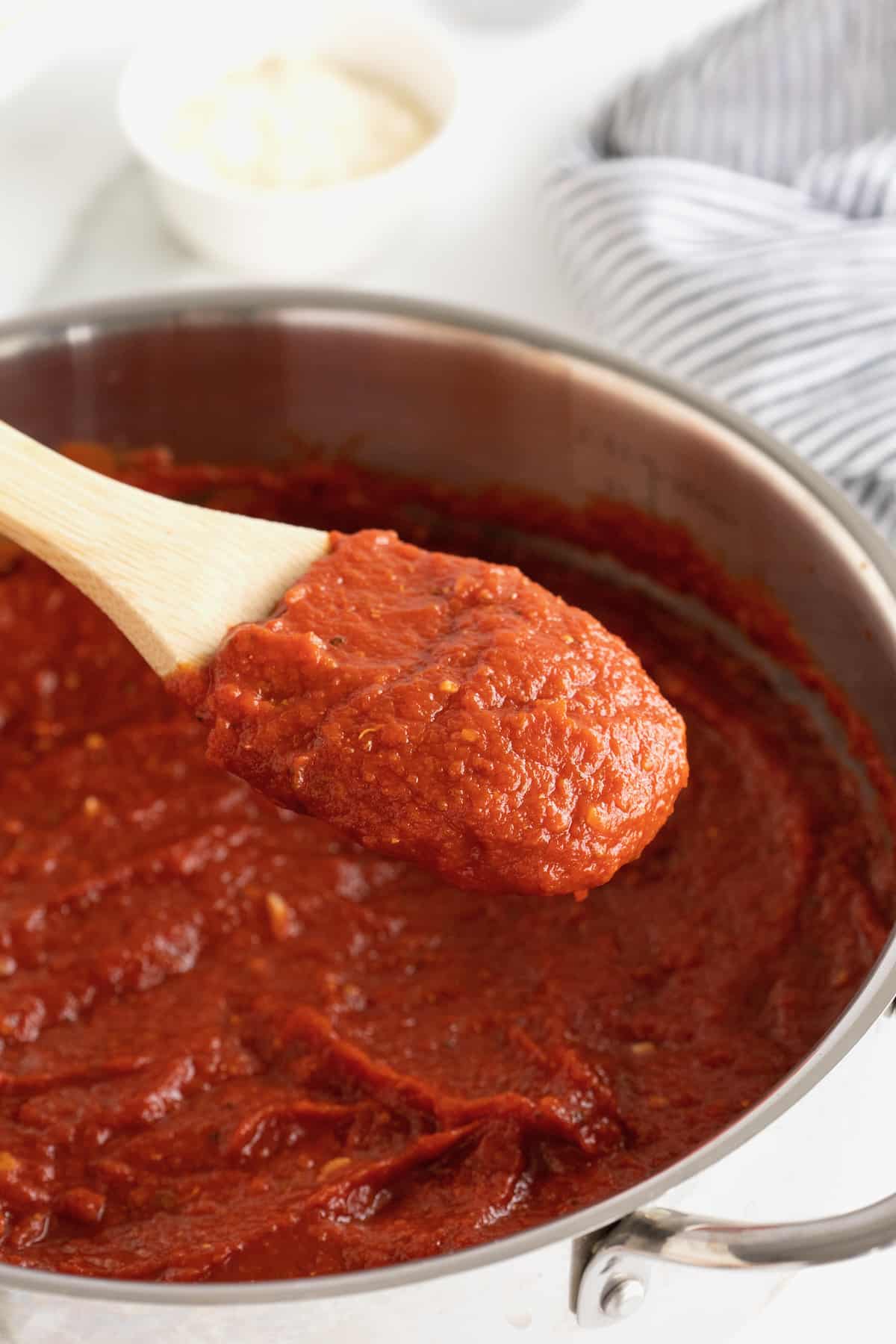 A large pot with red marinara sauce in it. A wooden spoon with a white handle is sticking out of the pot.