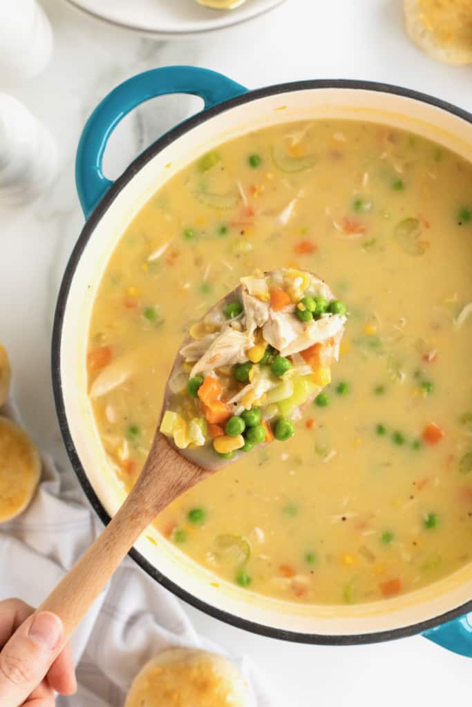 A blue Dutch oven filled with creamy Chicken Pot Pie Soup with a wooden spoon sticking out.