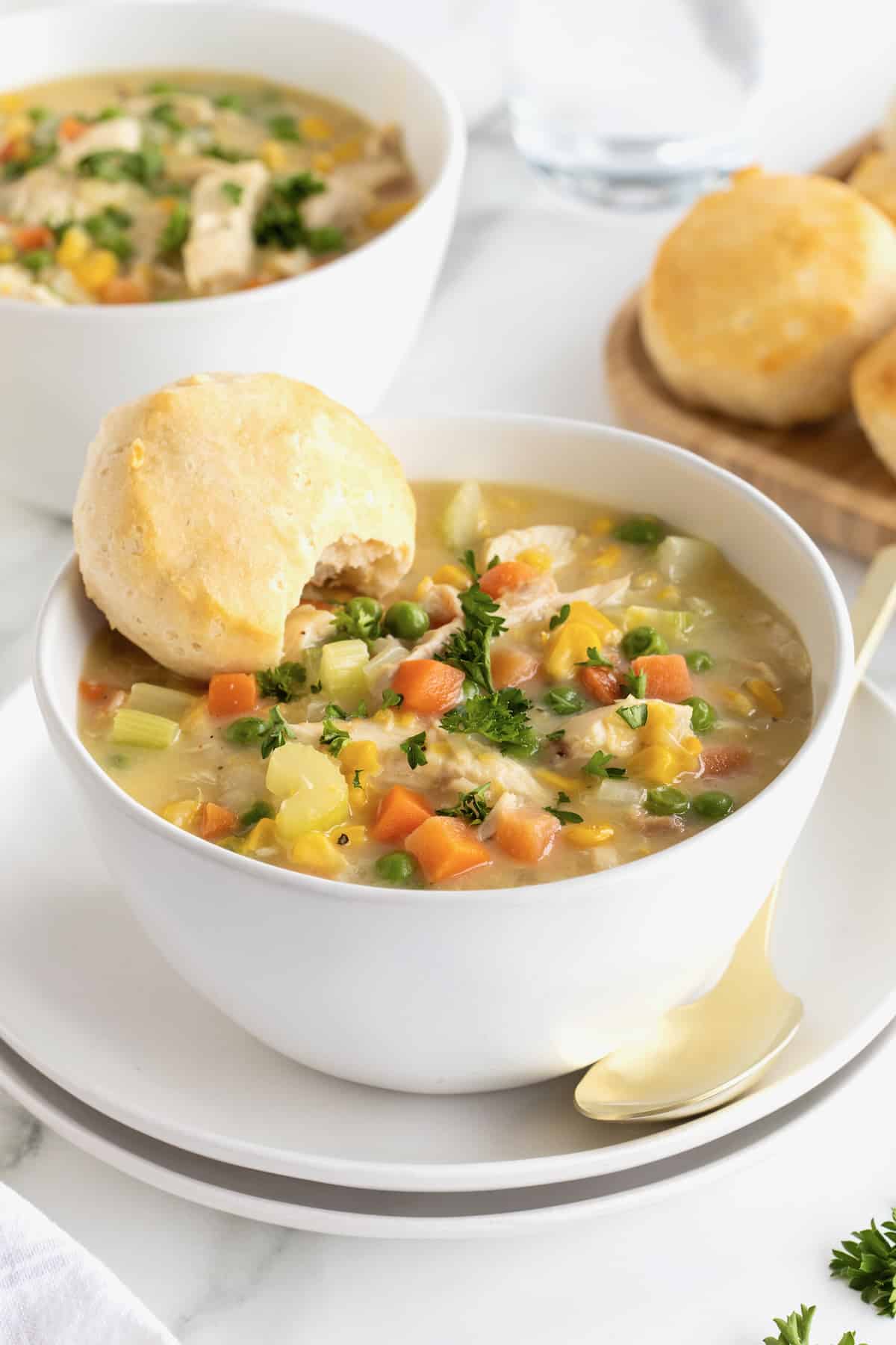A while ceramic bowl of chicken pot pie soup on a white plate with a spoon.