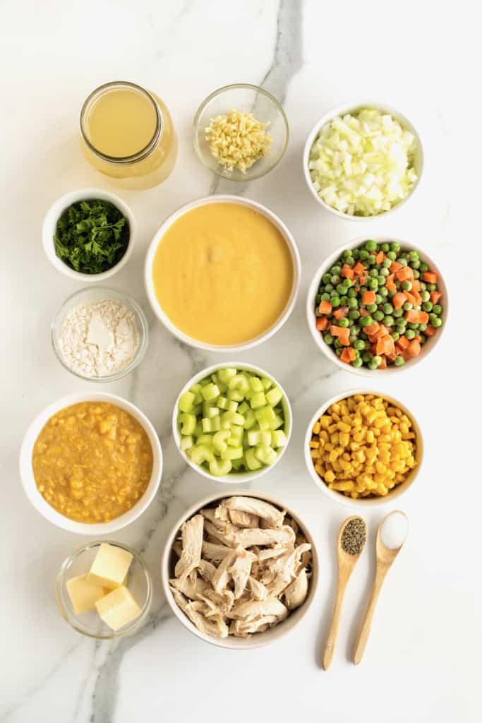 Ingredients for chicken pot pie soup in small white ceramic containers on a white marble counter.