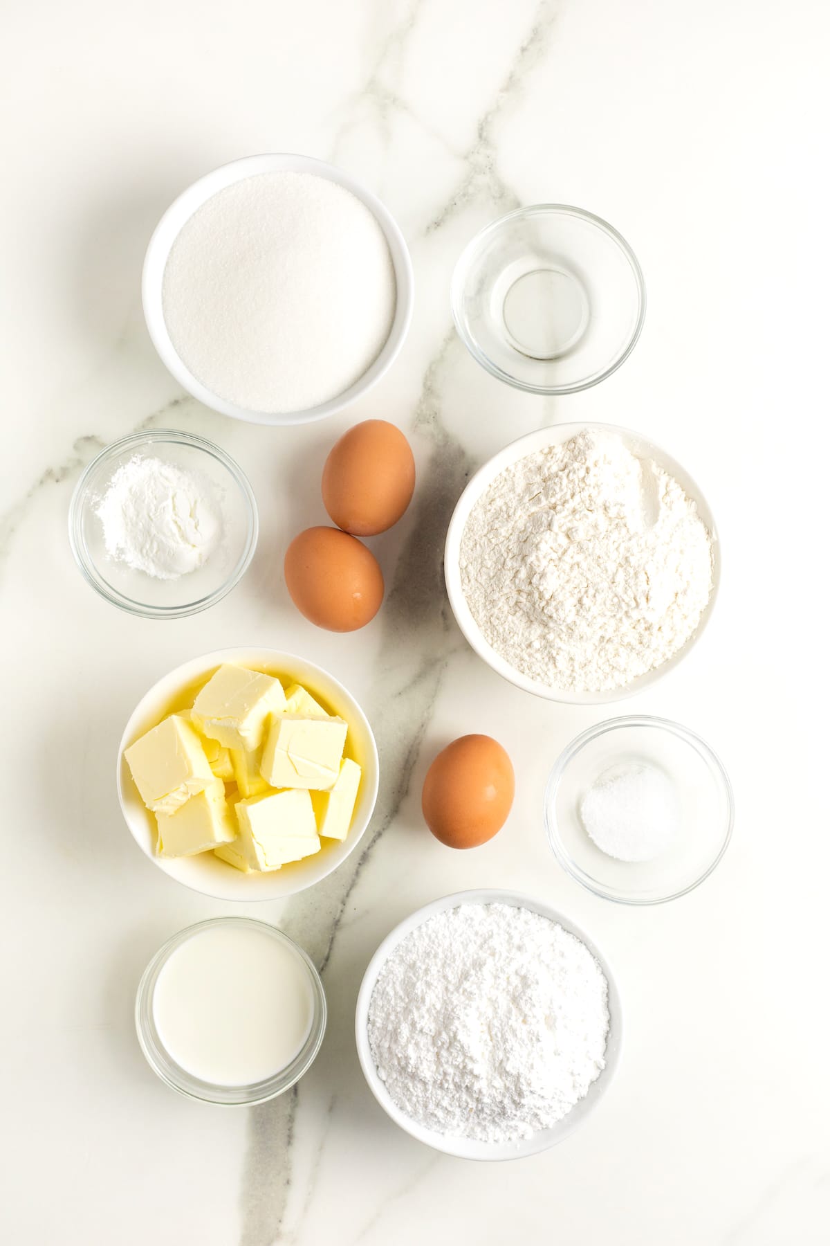 All the ingredients to make sugar cookies in small glass dishes on a white counter.