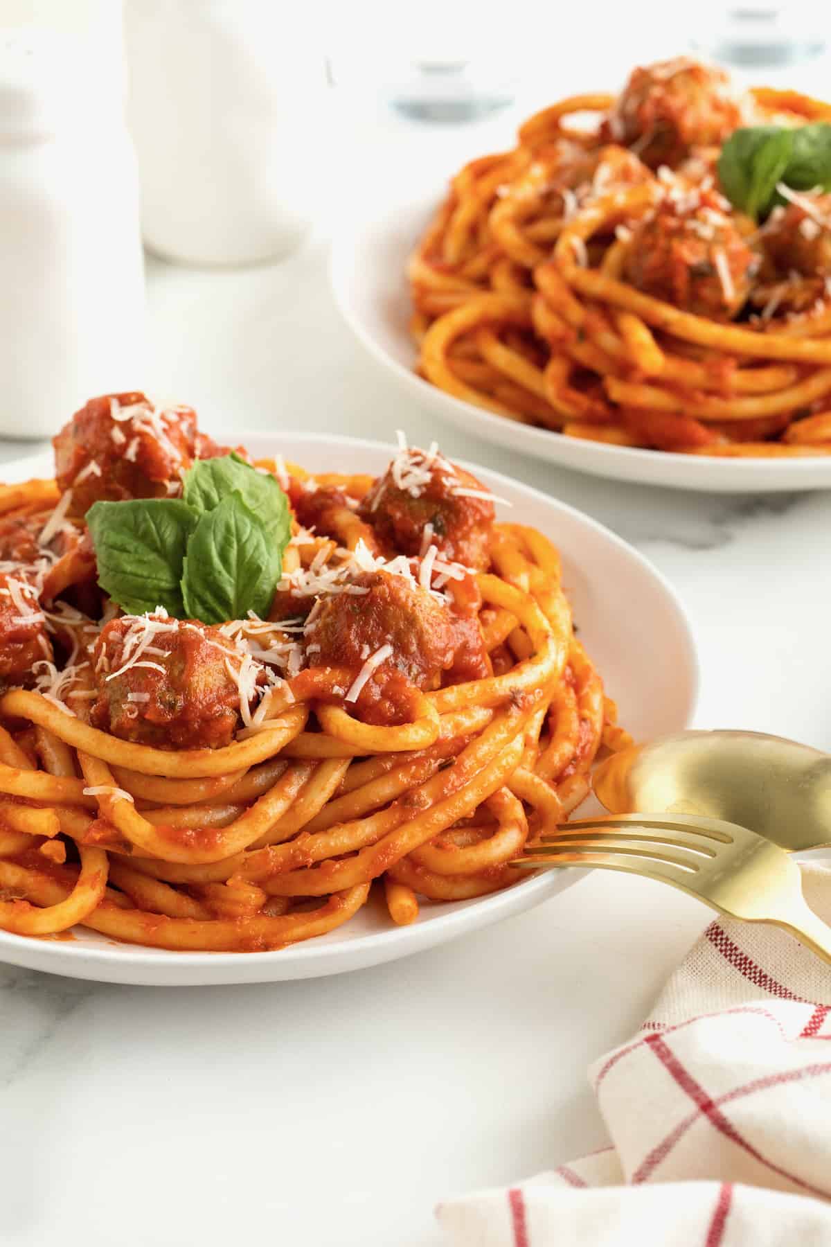 A large white plate with spaghetti and meatballs. The spaghetti is garnished with three fresh basil leaves.