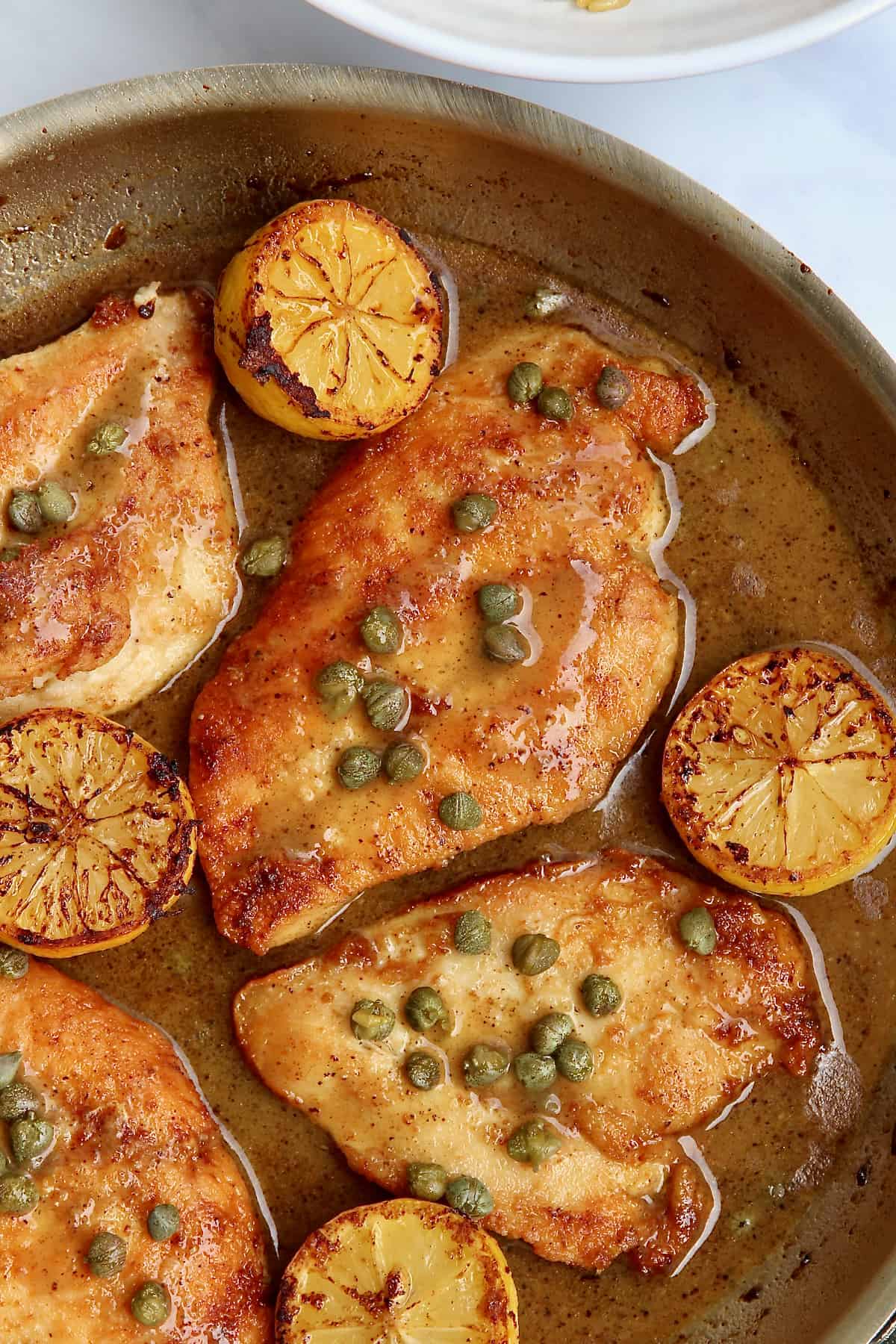 Chicken breast, lemon halves, capers and sauce in a skillet.