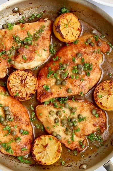 Chicken breast, lemon halves, capers and sauce in a skillet.