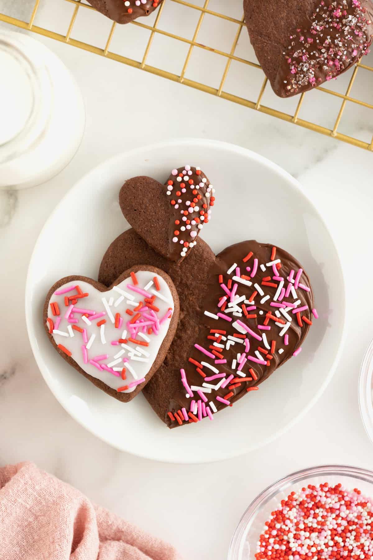A white plate with a small, medium and large heart shaped chocolate cookies with frosting and sprinkles.