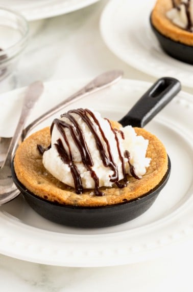 A chocolate chip cookie baked into a mini cast iron skillet topped with a scoop of vanilla ice cream and drizzled with chocolate syrup.