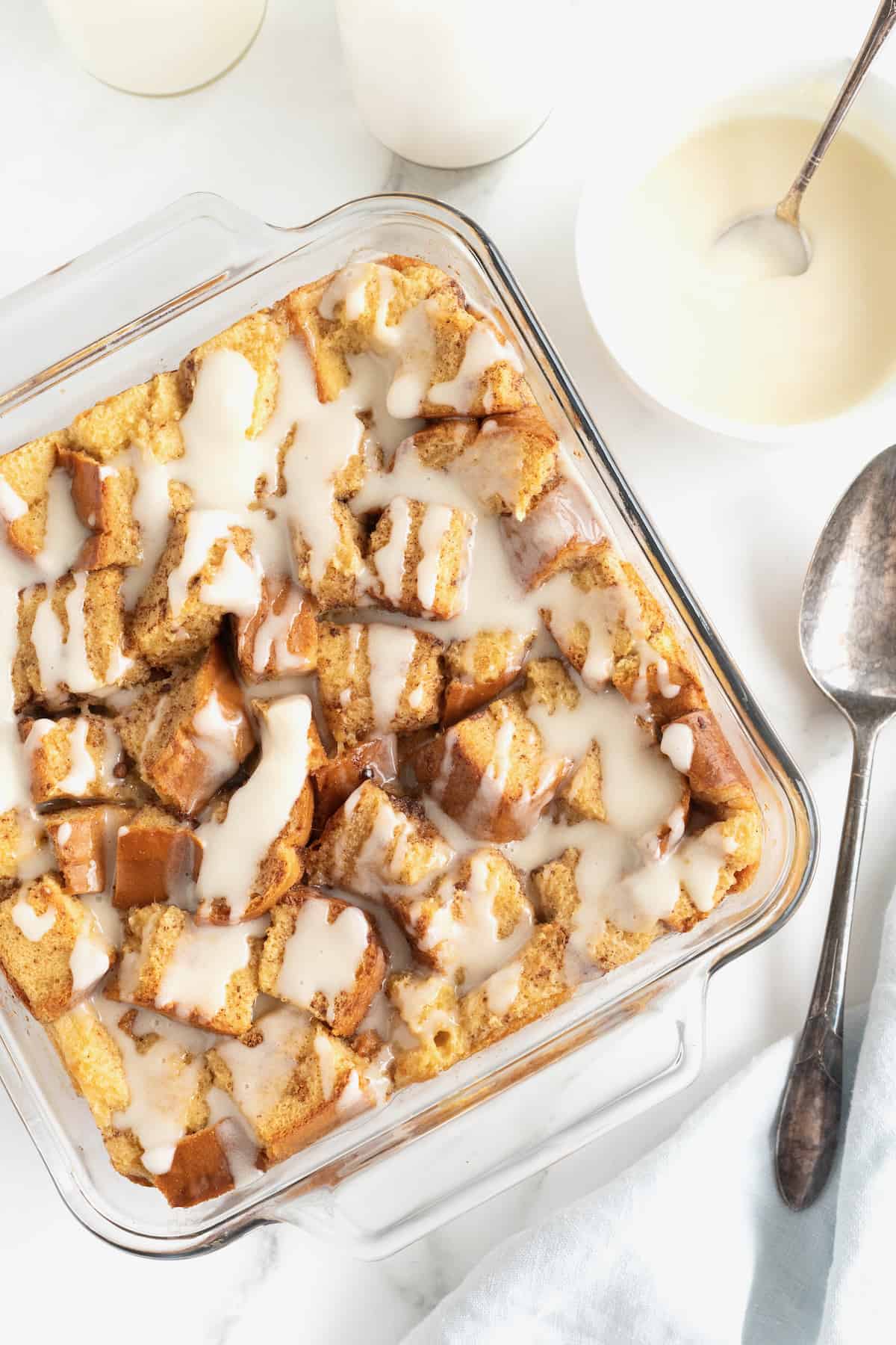 A square glass baking dish of bread pudding with white icing drizzled on top.