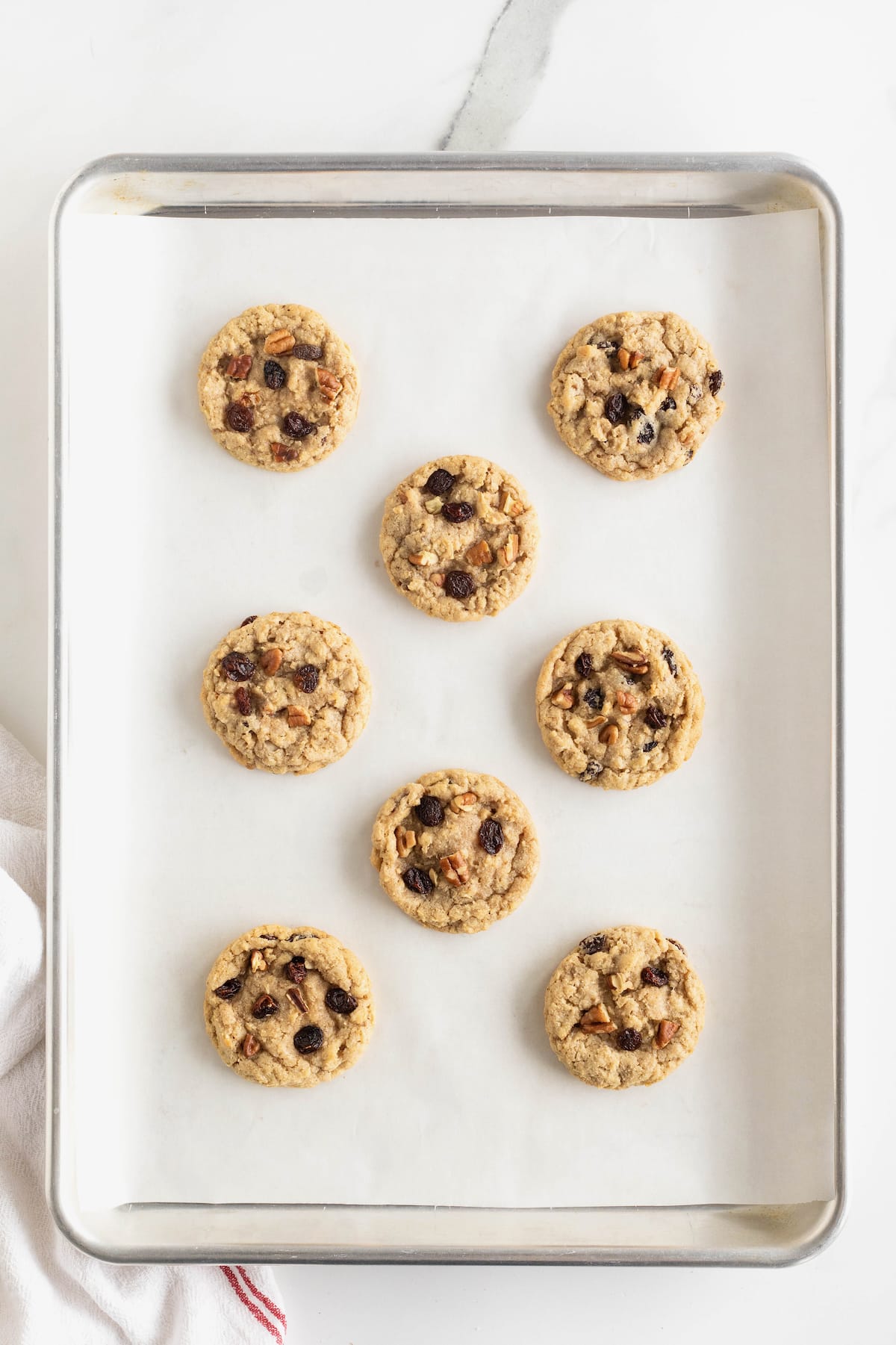 Eight baked oatmeal cookies on a parchment lined aluminum baking sheet.