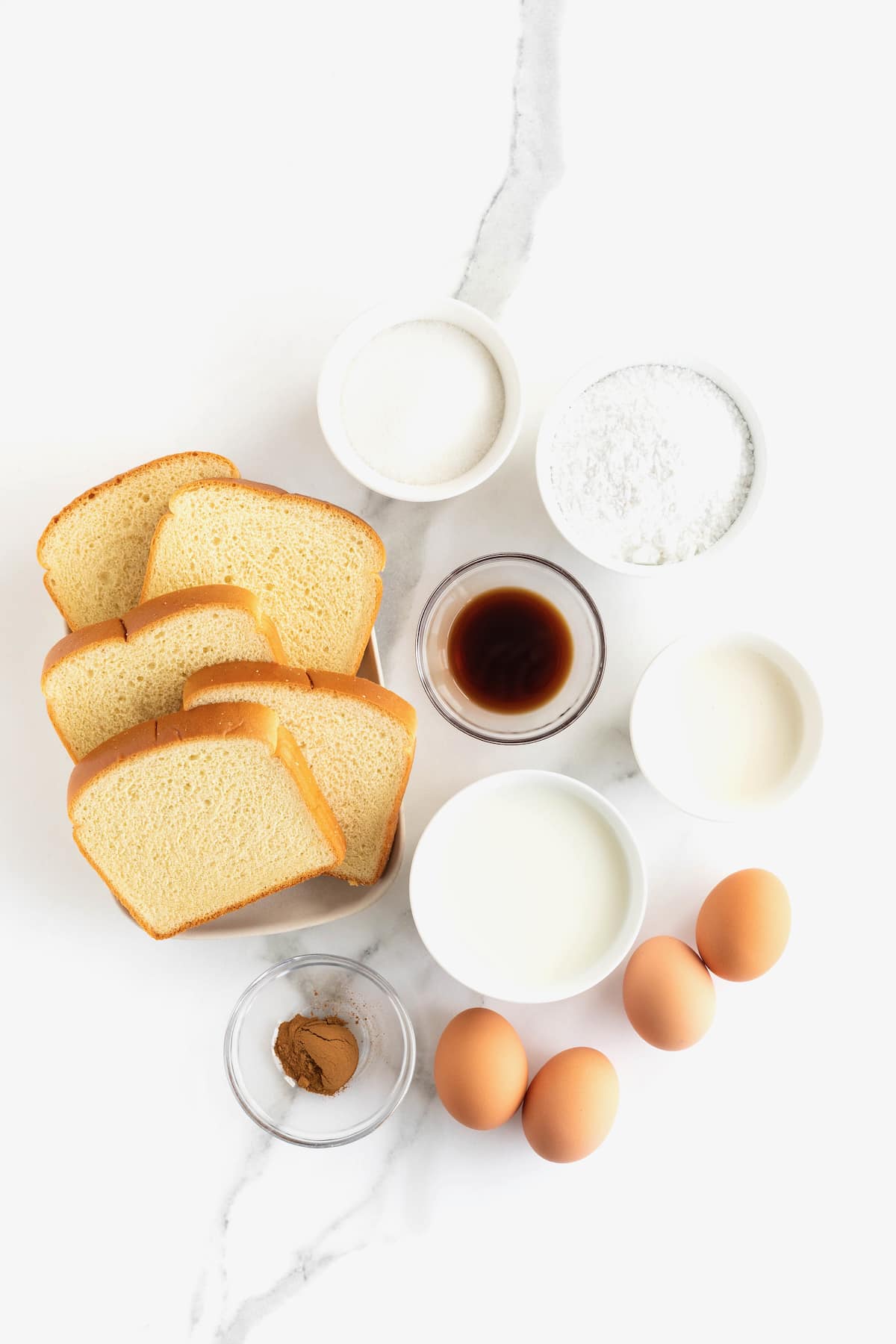 Ingredients to make bread pudding in small glass dishes on a white marble counter.