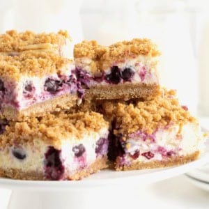 Four lemon blueberry cheesecake bars on a white cake stand.