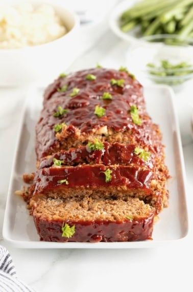 A meatloaf garnished with parsley on a rectangular, white rimmed serving plate.