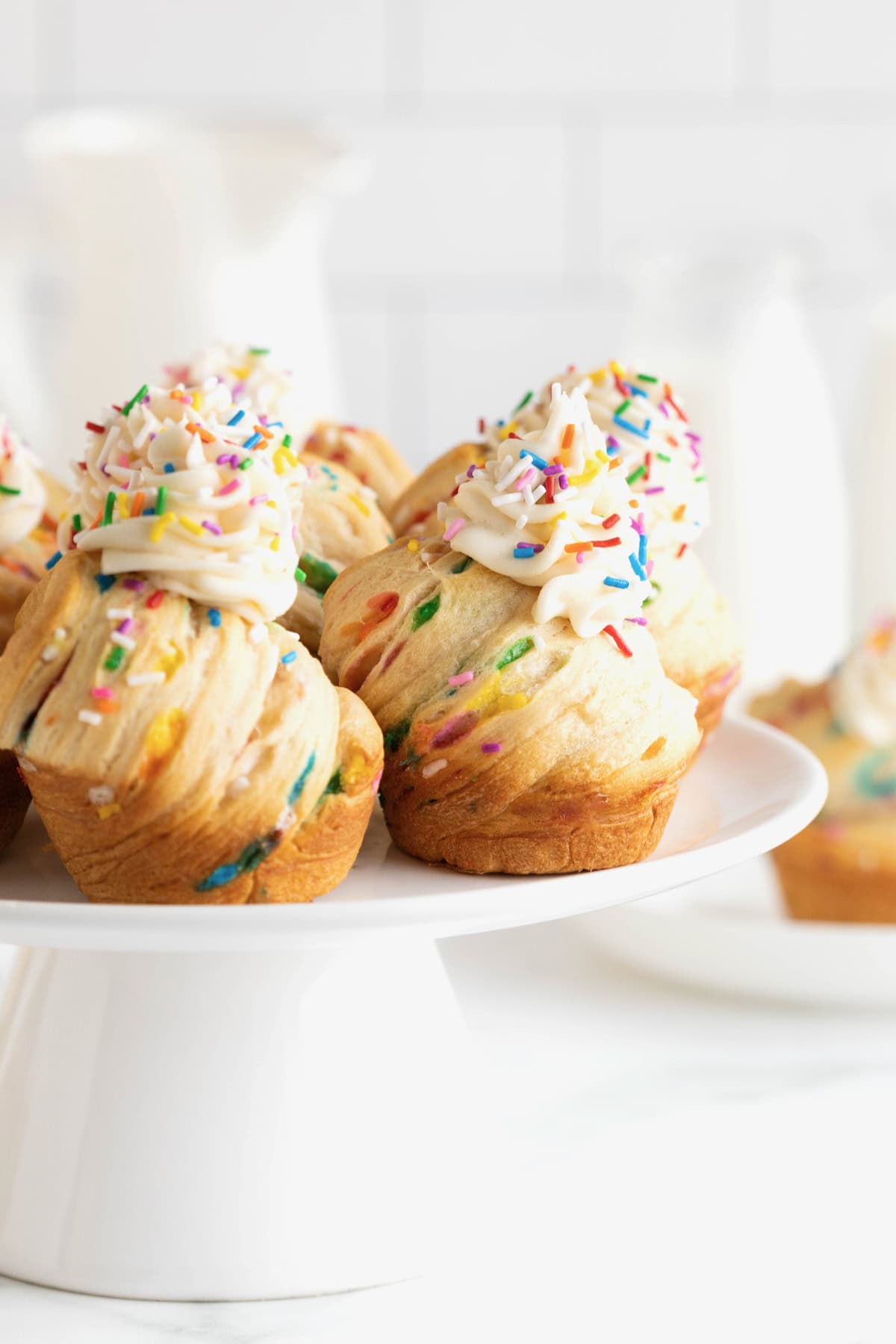 A white cake stand with five birthday confetti cruffins on top, as seen from the side.