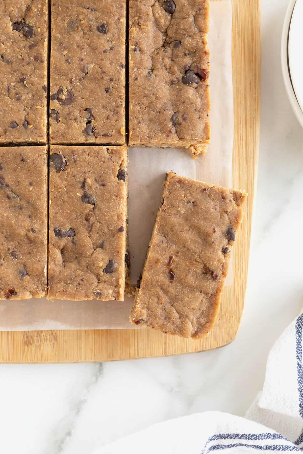 Six peanut butter chocolate chip breakfast bars on a parchment lined light wood cutting board.