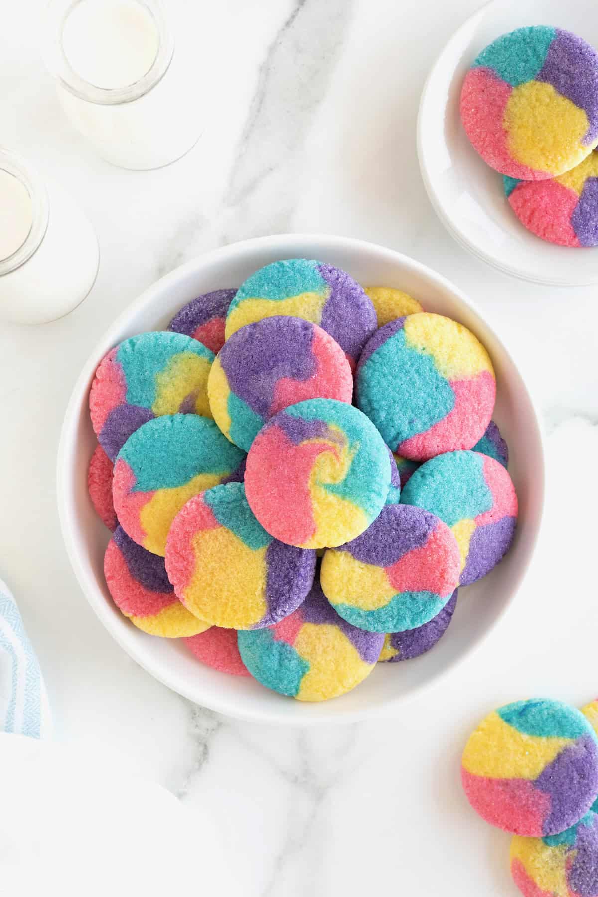 A large serving plate stacked with colorful sugar cookies with pink, purple, blue and yellow swirls in them.