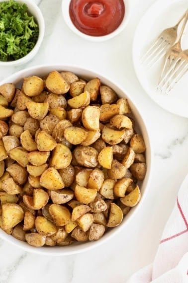 A large white serving dish of bite sized potato pieces on a white marble counter.