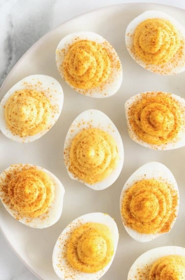 A large white serving plate of deviled eggs on a white marble counter.